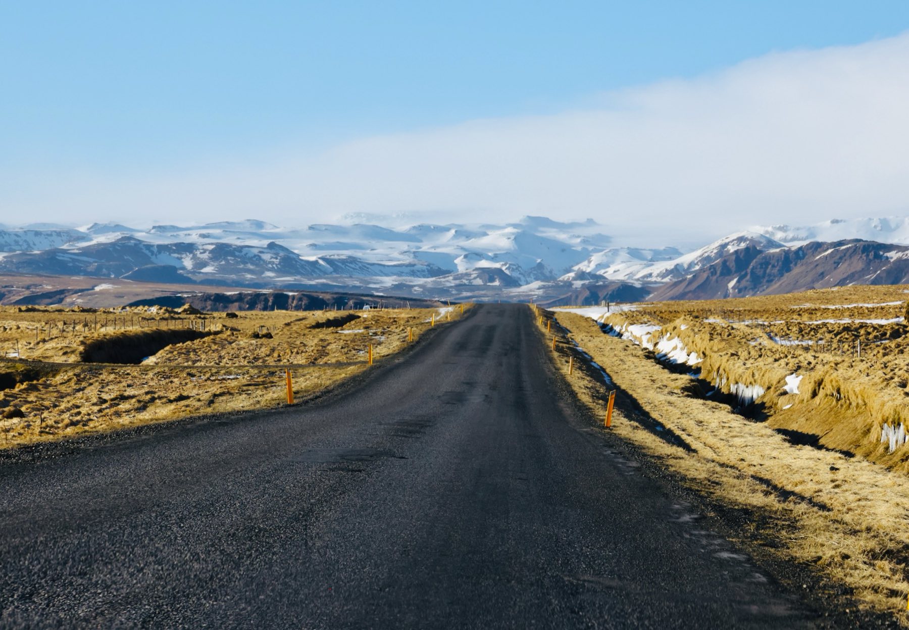 An empty road running straight toward distant snow-covered mountains.